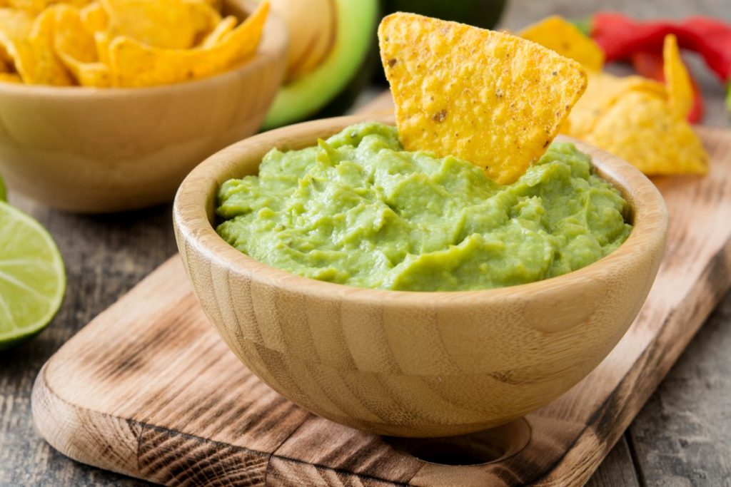 Guacamole: la ricetta della salsa messicana, calorie e varianti 4 vassoio di legno con sopra una ciotola di legno con guacamole e tacos
