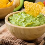 vassoio di legno con sopra una ciotola di legno con guacamole e tacos