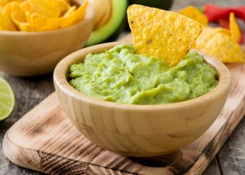 vassoio di legno con sopra una ciotola di legno con guacamole e tacos