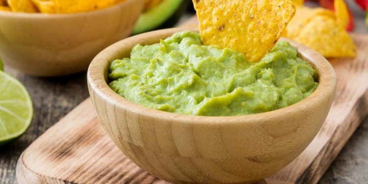 vassoio di legno con sopra una ciotola di legno con guacamole e tacos