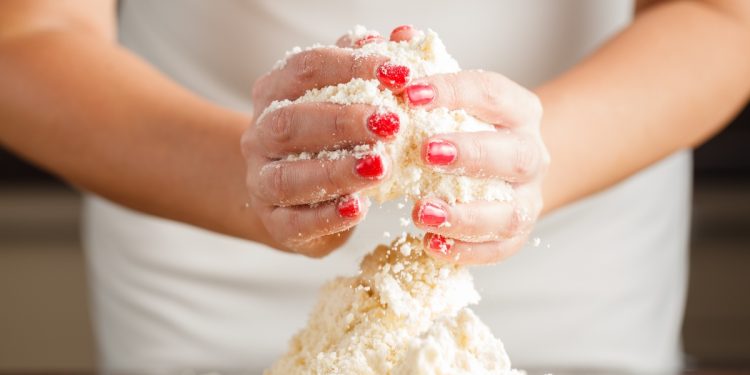 le mani di una donna mostrano come lavorare la farina per la pasta brisée per preparare le tue torte salate