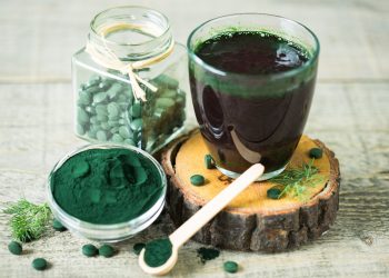 un bicchiere colmo di succo di spirulina con accanto delle compresse e della polvere sempre di alga spirulina