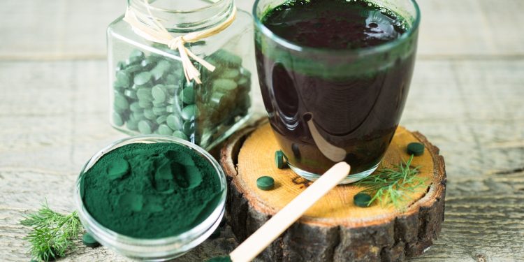 un bicchiere colmo di succo di spirulina con accanto delle compresse e della polvere sempre di alga spirulina
