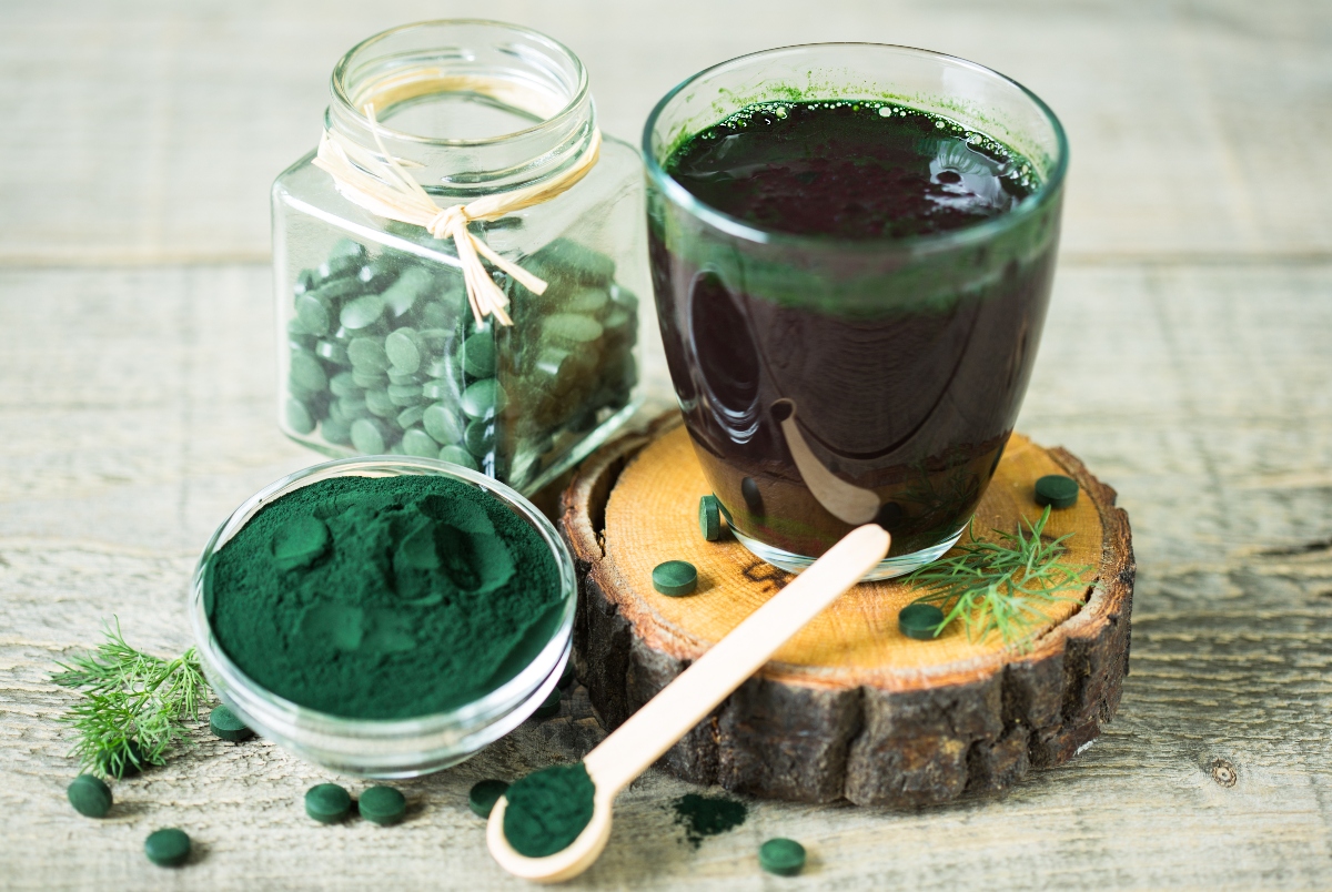 un bicchiere colmo di succo di spirulina con accanto delle compresse e della polvere sempre di alga spirulina