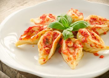 piatto bianco con 7 culurgiones sardi disposti a stella con foglie di basilico al centro