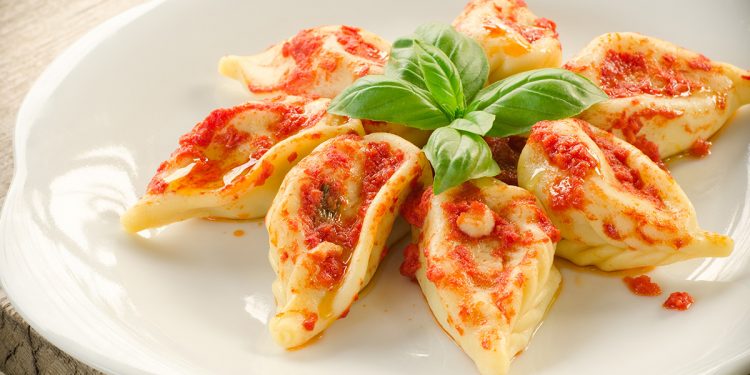 piatto bianco con 7 culurgiones sardi disposti a stella con foglie di basilico al centro