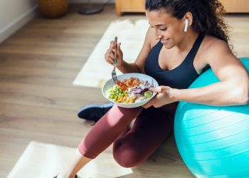 Donna in casa vestita da palestra, appoggiata su una fitball che mangia un insalata perché segue la dieta anticellulite
