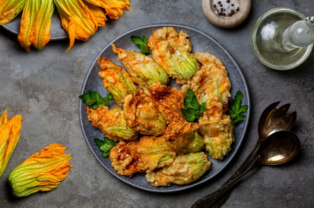 Fiori di zucca fritti senza pastella croccanti e leggeri 4 su tavolo da cucina di ardesia, piatto nero con fiori di zucca fritti e attorno fiori di zucca