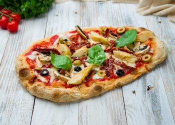 su tavolo di legno, pinsa romana con pomodori, funghi e rucola , accanto pomodorini