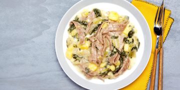 su piano di cucina grigio, piatto bianco con i pizzoccheri e accanto tovagliolo giallo forchetta e coltello