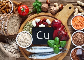 Alcuni alimenti su un tagliere in legno con al centro una piccola scritta con Cu, simbolo del rame