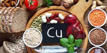 Alcuni alimenti su un tagliere in legno con al centro una piccola scritta con Cu, simbolo del rame