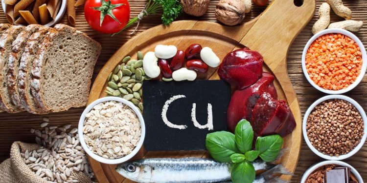 Alcuni alimenti su un tagliere in legno con al centro una piccola scritta con Cu, simbolo del rame