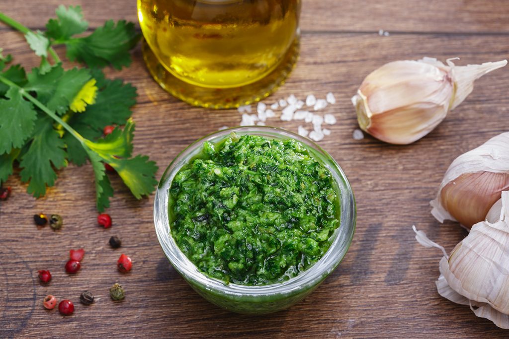 Salsa verde: ricetta facile di un classico piemontese 3 su tavolo di legno, ciotola di vetro con salsa verde alla Piemontese e attorno ingredienti come aglio, olio EVO, pepe e sale