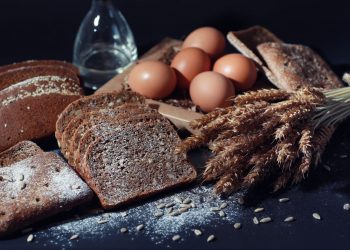 Delle fette di pane e delle spighe su un tavolo nero a rappresentare i prodotti che contengono glutine