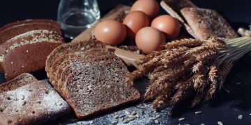 Delle fette di pane e delle spighe su un tavolo nero a rappresentare i prodotti che contengono glutine