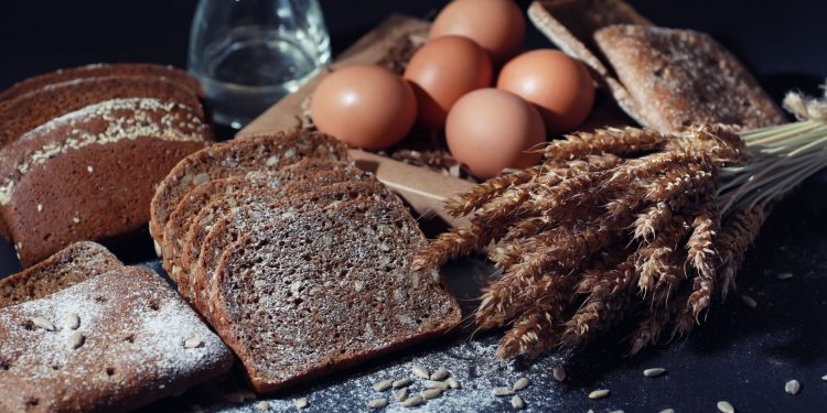 Delle fette di pane e delle spighe su un tavolo nero a rappresentare i prodotti che contengono glutine