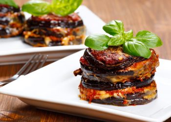 su tavolo di legno, piatto quadrato bianco con melanzane alla parmigiana