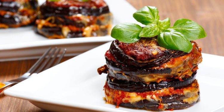 su tavolo di legno, piatto quadrato bianco con melanzane alla parmigiana