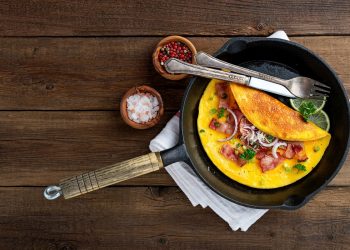 su tavolo di legno, padella con un omelette pronta con forchetta e coltello e accanto sale e pepe