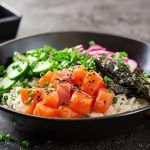 su tavolo di marmo: ciotola con poke bowl con alghe e salmone. Accanto bacchette cinese e dietro ciottola piccola con salsa di soia