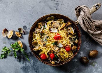 padella su un piano da cucina con spaghetti alle vongole e un canovaccio.