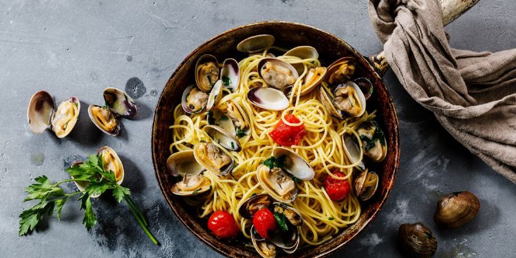 padella su un piano da cucina con spaghetti alle vongole e un canovaccio.