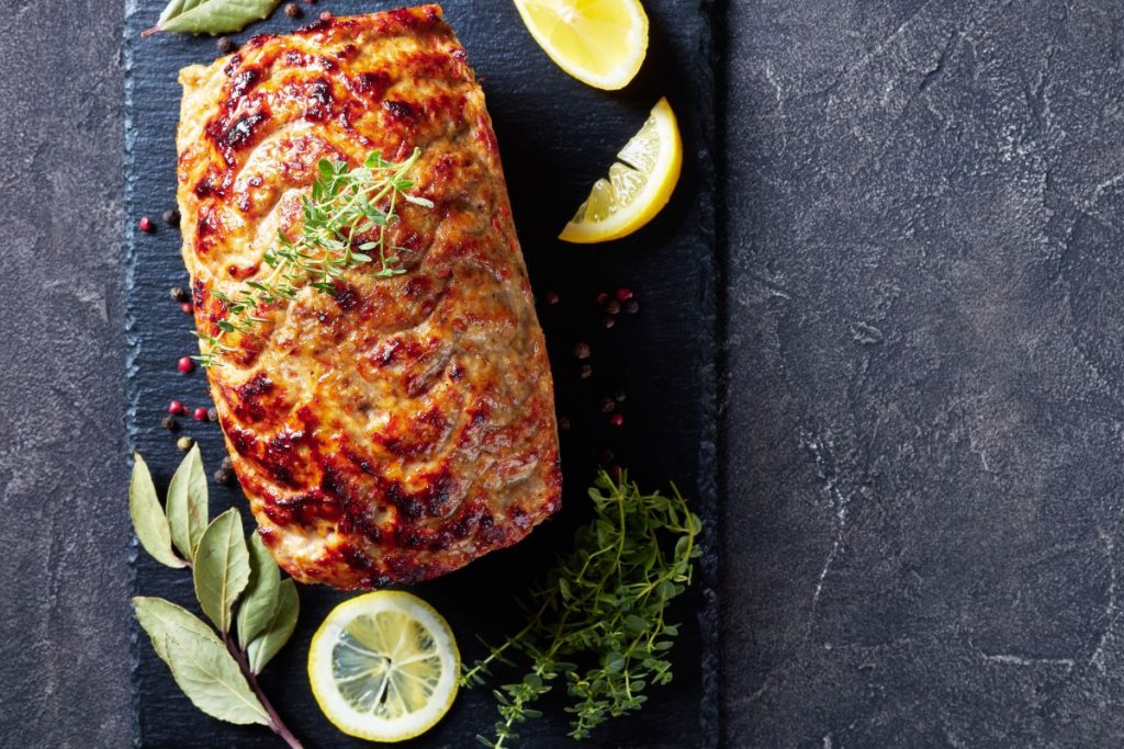 Polpettone di melanzane: la sfiziosa ricetta al forno 3 su sfondo nero, un polpettone di melanzane con erbe aromatiche e fette di limone