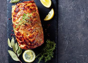 su sfondo nero, un polpettone di melanzane con erbe aromatiche e fette di limone