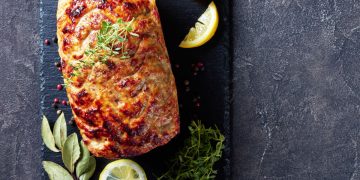 su sfondo nero, un polpettone di melanzane con erbe aromatiche e fette di limone