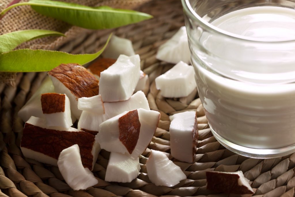 un bicchiere colmo di latte di cocco e dei pezzetti di cocco accanto