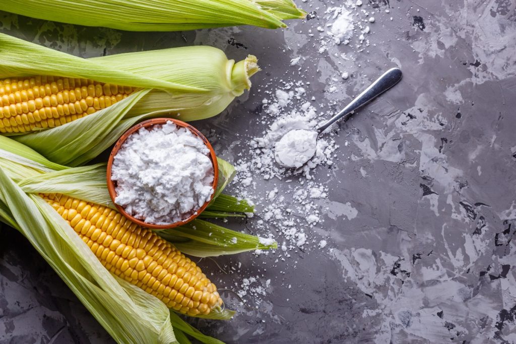 delle pannocchie di mais su un tavolo con accanto una ciotola piena di maizena