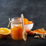 un vasetto di vetro pieno di marmellata di arance, anche spalmata su una fetta di pane, e metà arancia accanto