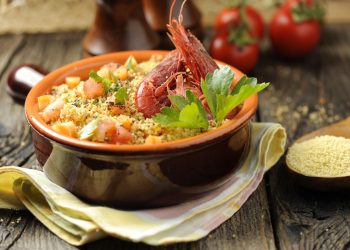 su tavolo di legno, un cucchiaio di legno con cous cous e tegame di terracotta