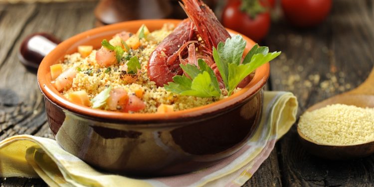 su tavolo di legno, un cucchiaio di legno con cous cous e tegame di terracotta