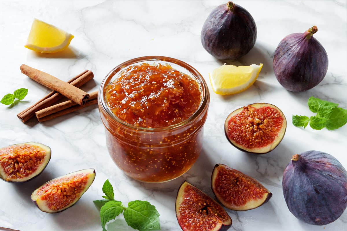 barattolo di vetro con marmellata di fichi, tre fichi neri e alcuni spicchi 