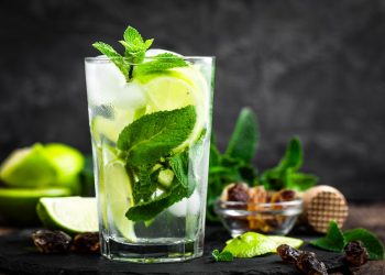 bicchiere con mojito e foglie di menta su base scura con spicchi di limone