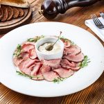 piatto rotondo bianco con fettine di vitella e al centro una ciotola di salsa tonnata