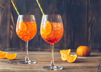 su base di legno due bicchieri con lo spritz e cannucce e spicchi di arancio intorno