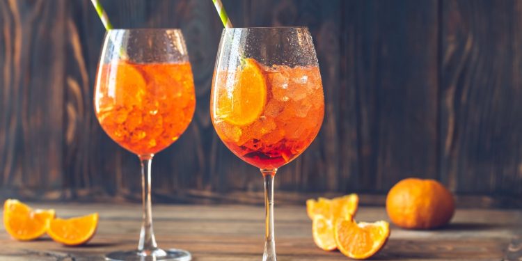 su base di legno due bicchieri con lo spritz e cannucce e spicchi di arancio intorno