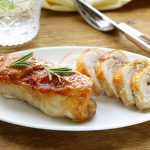 in primo piano su un piatto piano bianco, gli involtini di tacchino tagliati a fette e decorati con un rametto di rosmarino su una tavola di legno apparecchiata