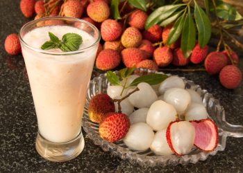 piatto in vetro con litchi sgusciati, e litchi interi sullo sfondo, un bicchiere con succo bianco