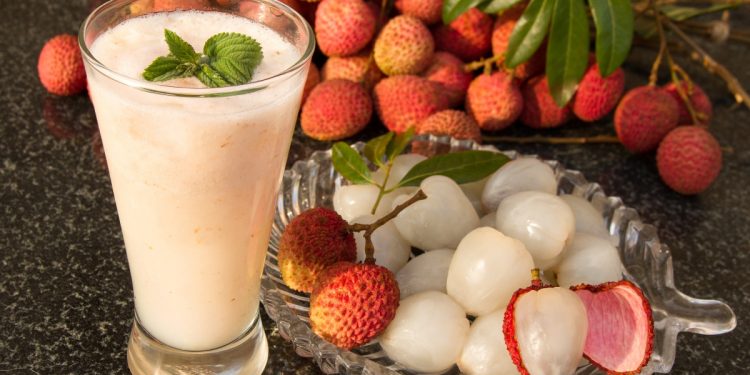 piatto in vetro con litchi sgusciati, e litchi interi sullo sfondo, un bicchiere con succo bianco