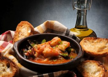 ciotola scura con il Cacciucco, crostini di pane sparsi intorno