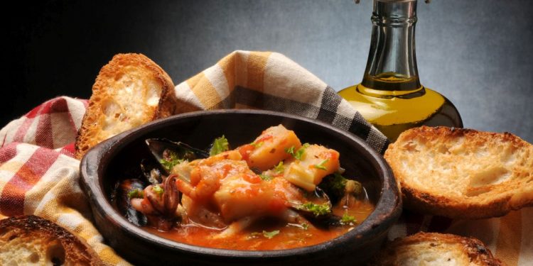 ciotola scura con il Cacciucco, crostini di pane sparsi intorno