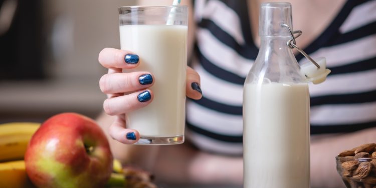 Una giovane donna tiene in mano un bicchiere di latte di mandorle