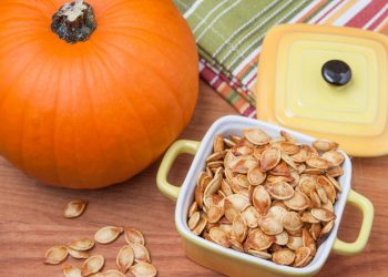 teglia con manici con semi di zucca tostati accanto a una grossa zucca