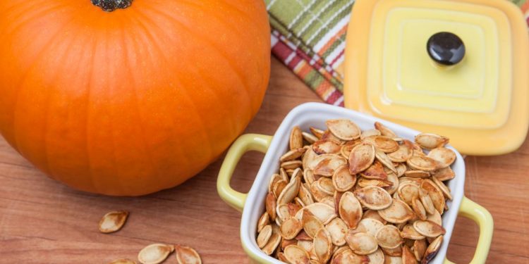 teglia con manici con semi di zucca tostati accanto a una grossa zucca