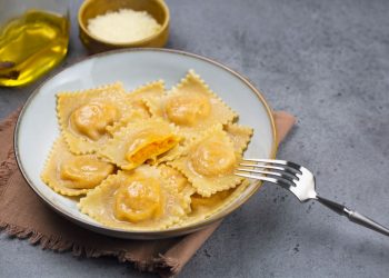 piatto fondo con tortelli di zucca, forchetta, olio e parmigiano accanto