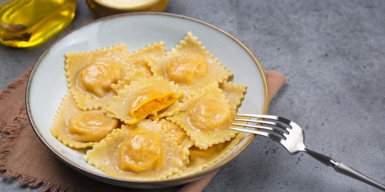 piatto fondo con tortelli di zucca, forchetta, olio e parmigiano accanto